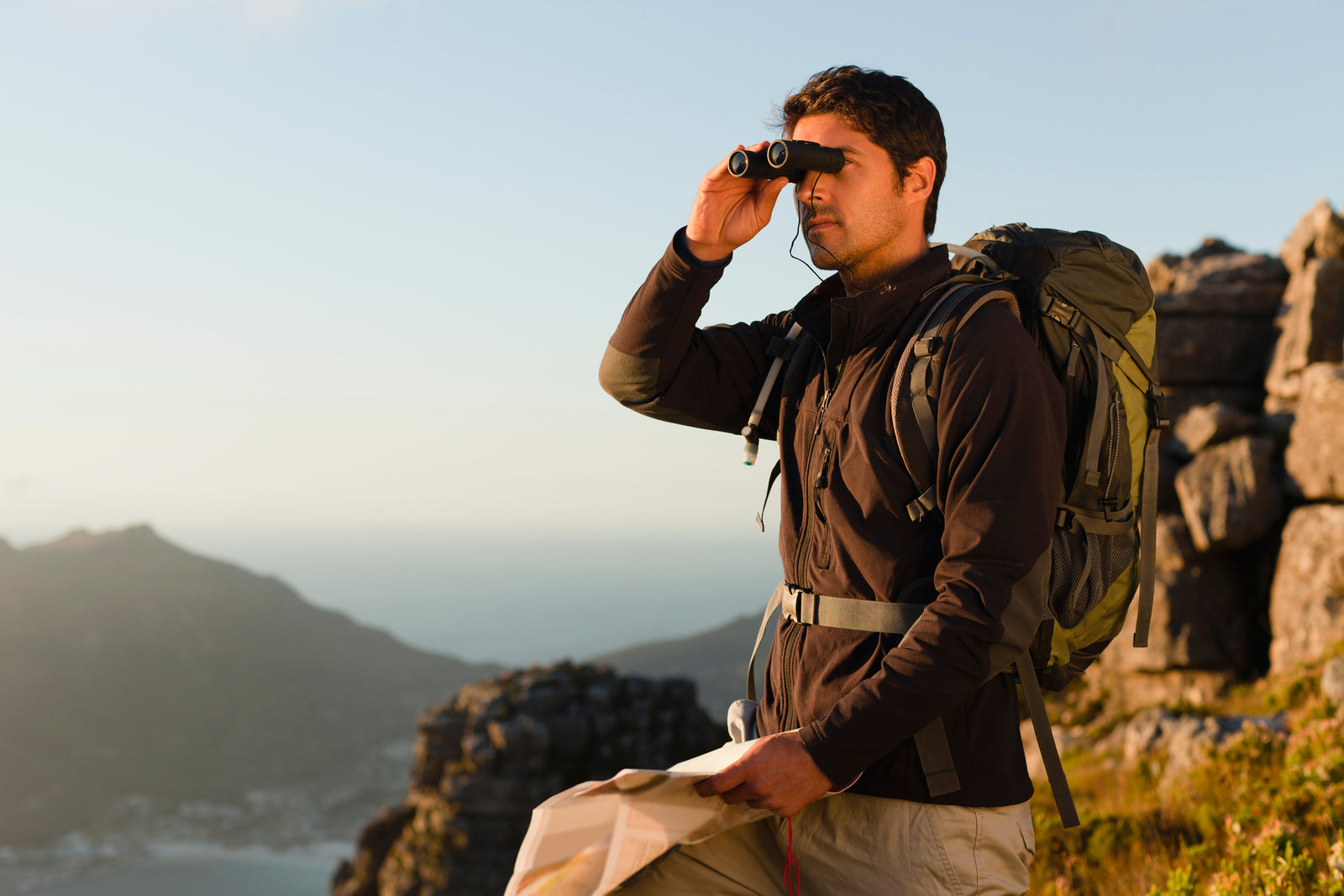 Mid-40s hiker using compact binoculars while navigating a rocky hillside trail