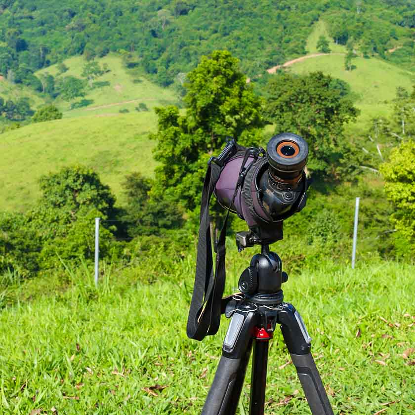 A professional spotting scope mounted on a sturdy tripod set against the lush green backdrop of a rolling hillside, capturing the essence of nature observation and outdoor exploration