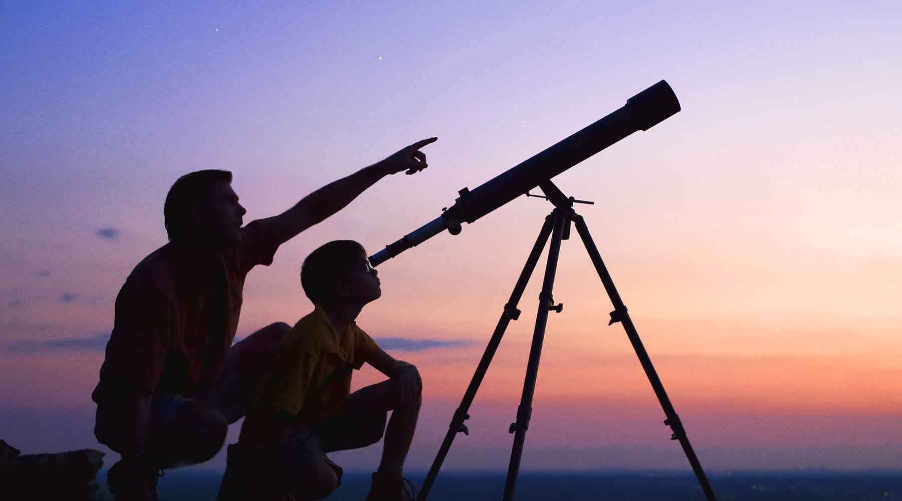 Two enthusiasts enjoying a stargazing adventure with a professional telescope during twilight, showcasing the quality equipment available at our optics store for astronomy lovers